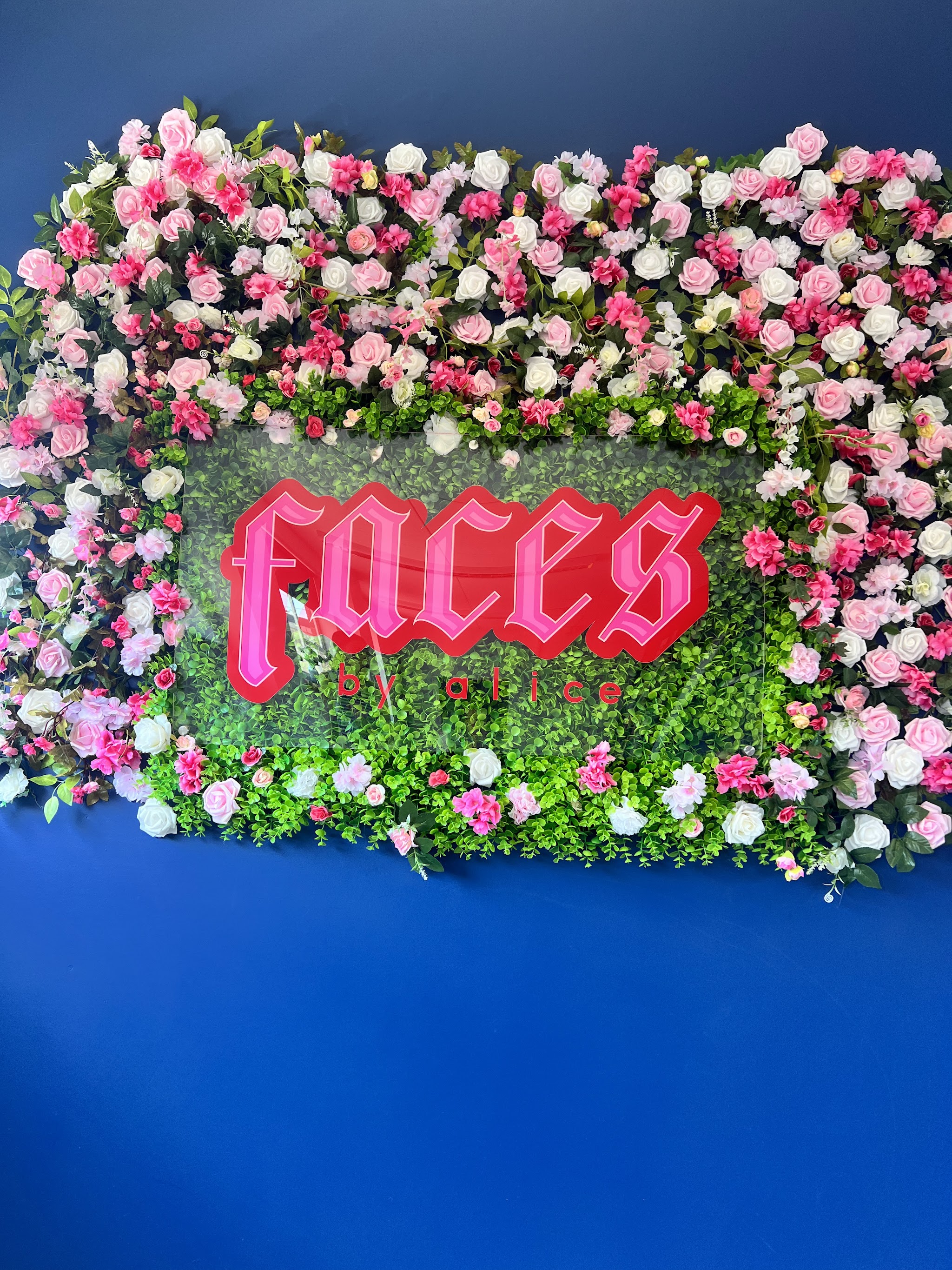 The FACES by Alice flower wall, pink and white roses around the red neon faces by alice sign